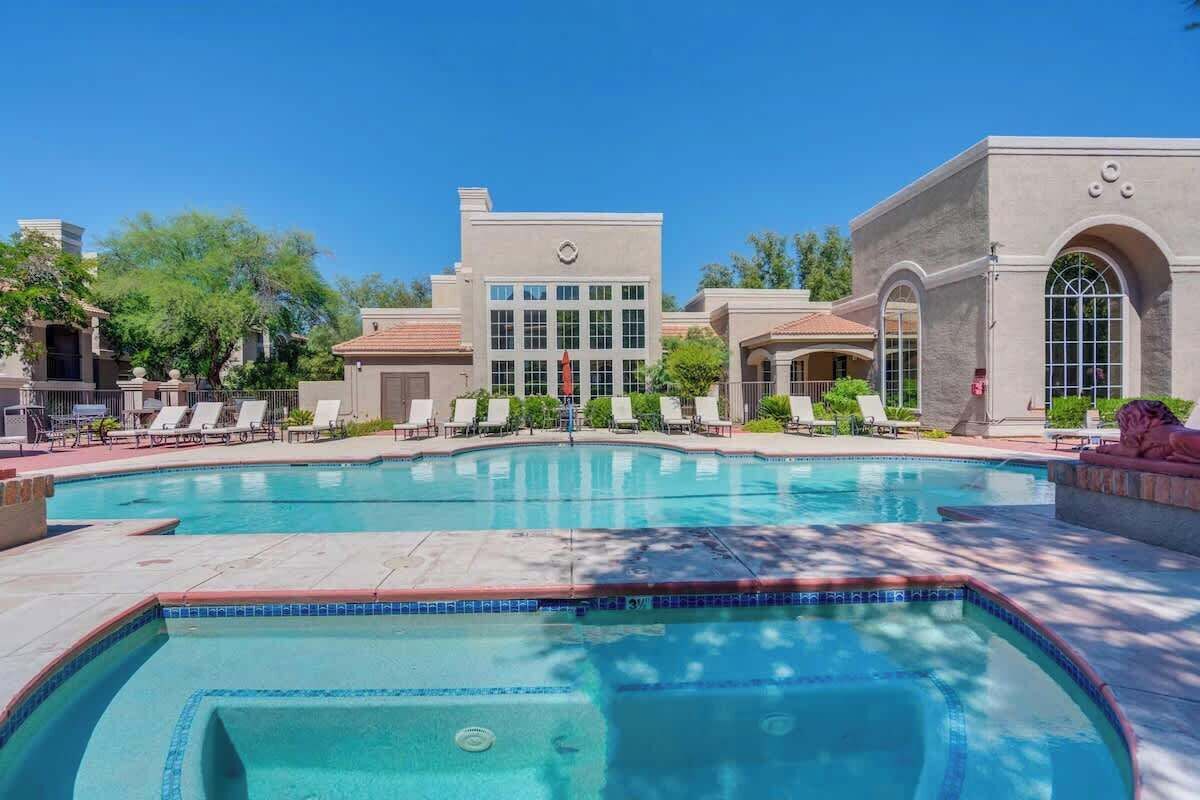 A hotel with a large pool, lounge chairs, and a building with a modern design.