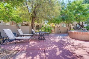 Eine Terrasse im Freien mit Lounge-Möbeln und einem Tisch, umgeben von Bäumen und einem Gebäude mit Bögen.