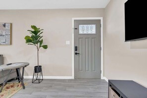 A room with a grey door, a potted plant, a round table, and a flat-screen TV mounted on the wall. - Modern Central Location-10 mins from U of A (Tucson)
