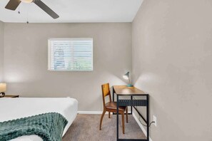 Une chambre à coucher comprenant un lit, un bureau, une chaise, un ventilateur de plafond et une fenêtre avec des stores.