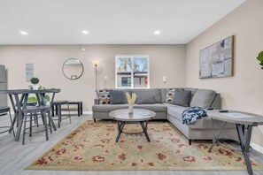 A living room with a sofa, coffee table, and dining area with chairs. - Modern Central Location-10 mins from U of A (Tucson)