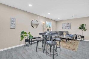 A modern living room with a round dining table, bar stools, a sofa, and a coffee table. There is a large mirror on the wall, a potted plant, and a framed quote. - Modern Central Location-10 mins from U of A (Tucson)