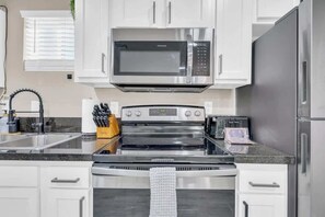Una cocina con microondas, horno y refrigerador de acero inoxidable, gabinetes blancos y encimera de granito.