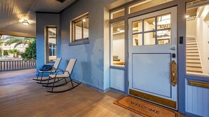 A hotel entrance with a blue exterior, a welcome mat, a set of rocking chairs, and a staircase leading inside. - Famous Historic Big Blue House (Tucson)