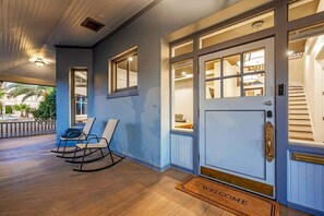 A hotel entrance with a blue exterior, a welcome mat, a set of rocking chairs, and a staircase leading inside. - Famous Historic Big Blue House (Tucson)