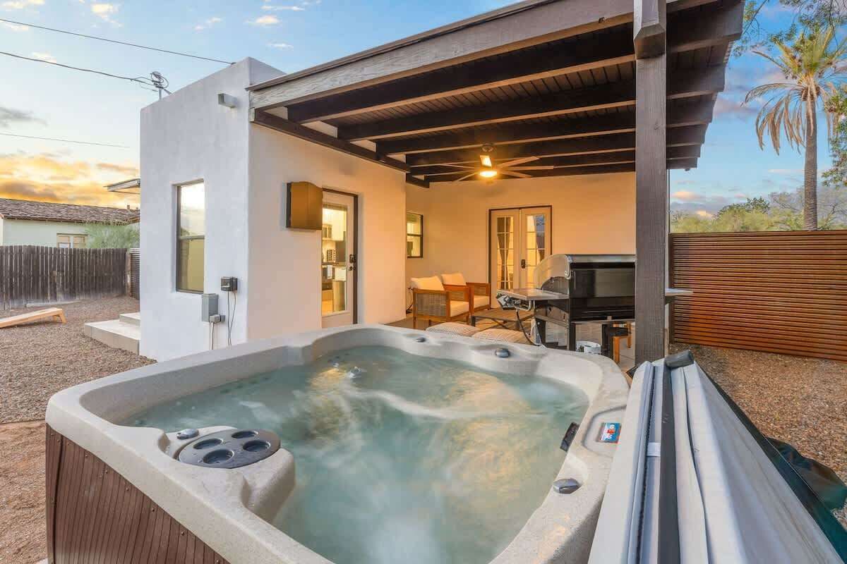 A hot tub in a covered outdoor area with a modern house in the background.