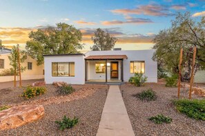 A modern two-story house with a front entrance, large windows, and a gravel driveway. - Renovated Adobe with Hot Tub-Close to U of A (Tucson)