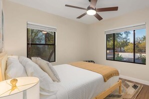 A bedroom with a bed, a ceiling fan, two windows, and a nightstand with a lamp. - Renovated Adobe with Hot Tub-Close to U of A (Tucson)