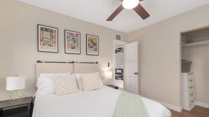 Ein Schlafzimmer mit Bett, Nachttischen, Deckenventilator und begehbarem Kleiderschrank.