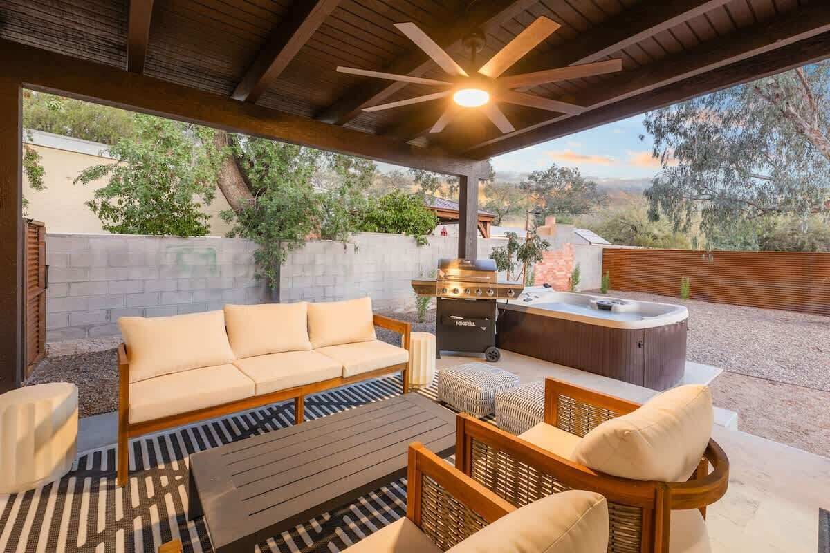 An outdoor patio with a sofa, ottomans, a grill, and a hot tub.