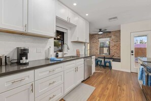 A modern kitchen with white cabinets, a coffee machine, and a brick wall. - Renovated Adobe with Hot Tub-Close to U of A (Tucson)