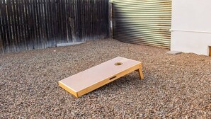 Ein Garten mit einem hölzernen Gesellschaftsspiel auf Kies, einem Holzzaun und einem Metalltor.