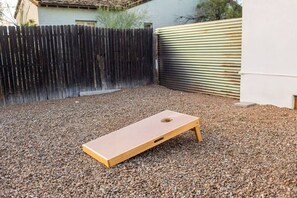 A backyard with a wooden board game on gravel, a wooden fence, and a metal gate. - Renovated Adobe with Hot Tub-Close to U of A (Tucson)