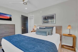A modern bedroom with a large bed, a ceiling fan, a nightstand with a lamp, and artwork on the walls. - Stunning View w/Heated Pool! (Tucson)