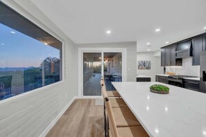 A modern kitchen with a large island, dark cabinets, and a view through a glass door to an outdoor deck. - Stunning View w/Heated Pool! (Tucson)