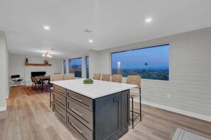 A modern kitchen with a large island, dining area with chairs, and large windows offering a city view. - Stunning View w/Heated Pool! (Tucson)
