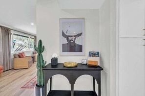 Ein modernes Wohnzimmer mit großem Fenster, einem Kakteen, einem gerahmten Kunstwerk und einem kleinen Tisch mit Tablett.