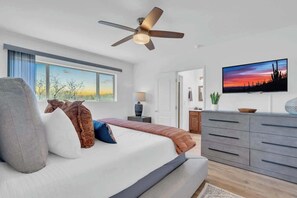 A modern bedroom with a bed, a ceiling fan, a TV, and a large window. - Desert Vibes with Pool, Sauna & Game Room! (Tucson)
