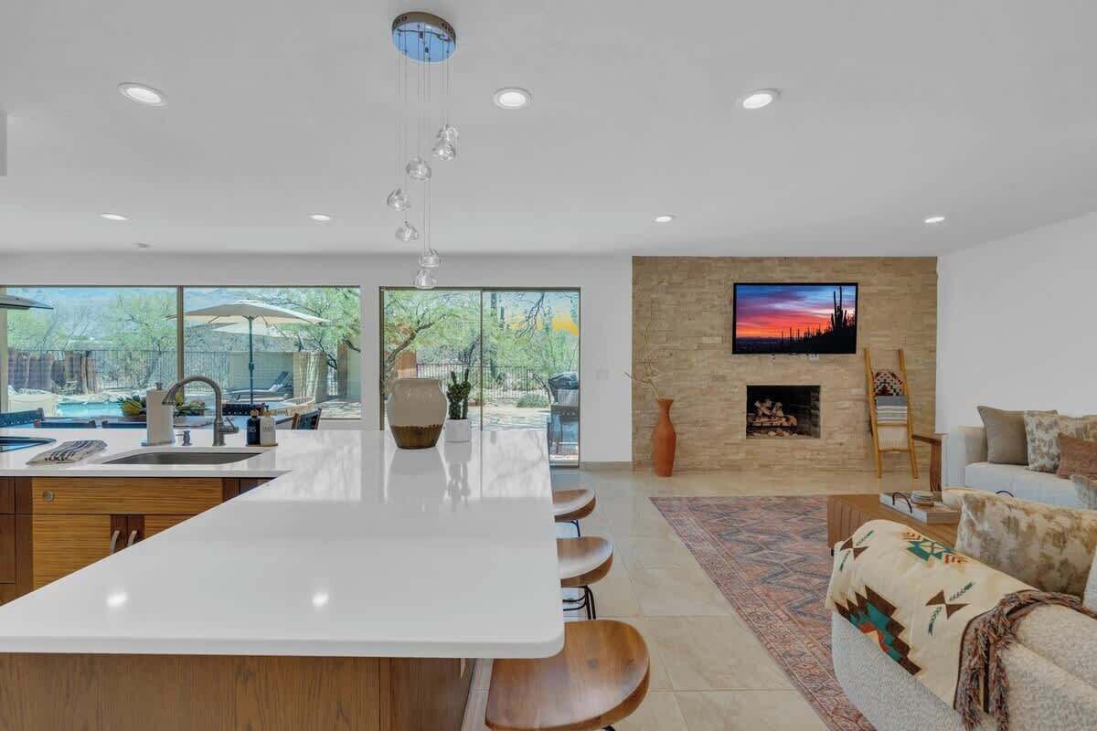 A modern kitchen with a central island, a dining area with bar stools, a fireplace, and a large TV on the wall.