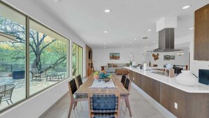 A modern kitchen with a dining area, large windows, and a view of trees. - Desert Vibes with Pool, Sauna & Game Room! (Tucson)