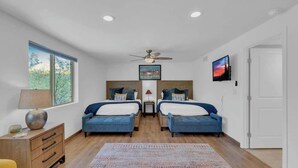 A bedroom with two beds, a ceiling fan, a TV, and a window with a view of trees. - Desert Vibes with Pool, Sauna & Game Room! (Tucson)