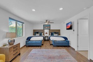 Ein Schlafzimmer mit zwei Betten, einem Deckenventilator, einem Fernseher und einem Fenster mit Blick auf Bäume.