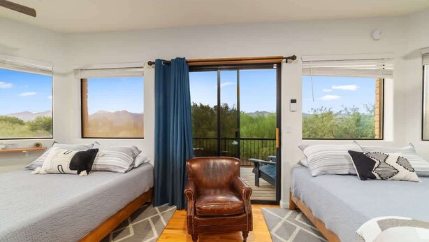 A room with two beds, a wooden chair, and large windows. - Modern Loft with Pool & Hot Tub-Views! (Tucson)