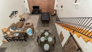 A living room with a fireplace, a pool table, a dining table with chairs, and a staircase with a railing. - Modern Loft with Pool & Hot Tub-Views! (Tucson)