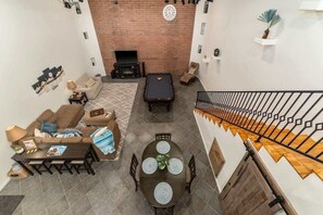 Ein Wohnzimmer mit Kamin, Billardtisch, Esstisch mit Stühlen und einer Treppe mit Geländer.