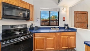 A kitchen with wooden cabinets, a black microwave, a stove, and a large window with blinds. - Modern Loft with Pool & Hot Tub-Views! (Tucson)
