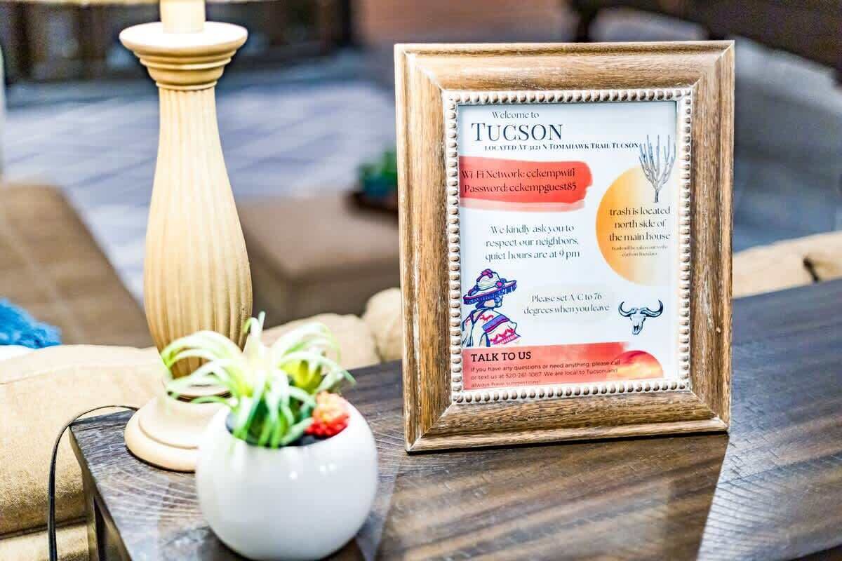 Un panneau d’accueil encadré indiquant les informations relatives au Wi-Fi, un cactus et une bougie, le tout posé sur une table en bois.