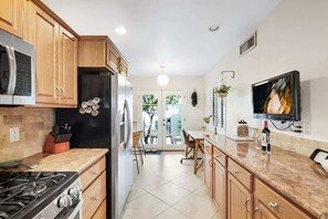 A kitchen with wooden cabinets, a gas stove, a black refrigerator, and a dining area with a table and chairs. - Pool & Pet Friendly-Walk to Udall Park (Tucson)