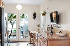 A kitchen with a large island, a dining area with chairs, a television mounted on the wall, and a view through the glass doors. - Pool & Pet Friendly-Walk to Udall Park (Tucson)
