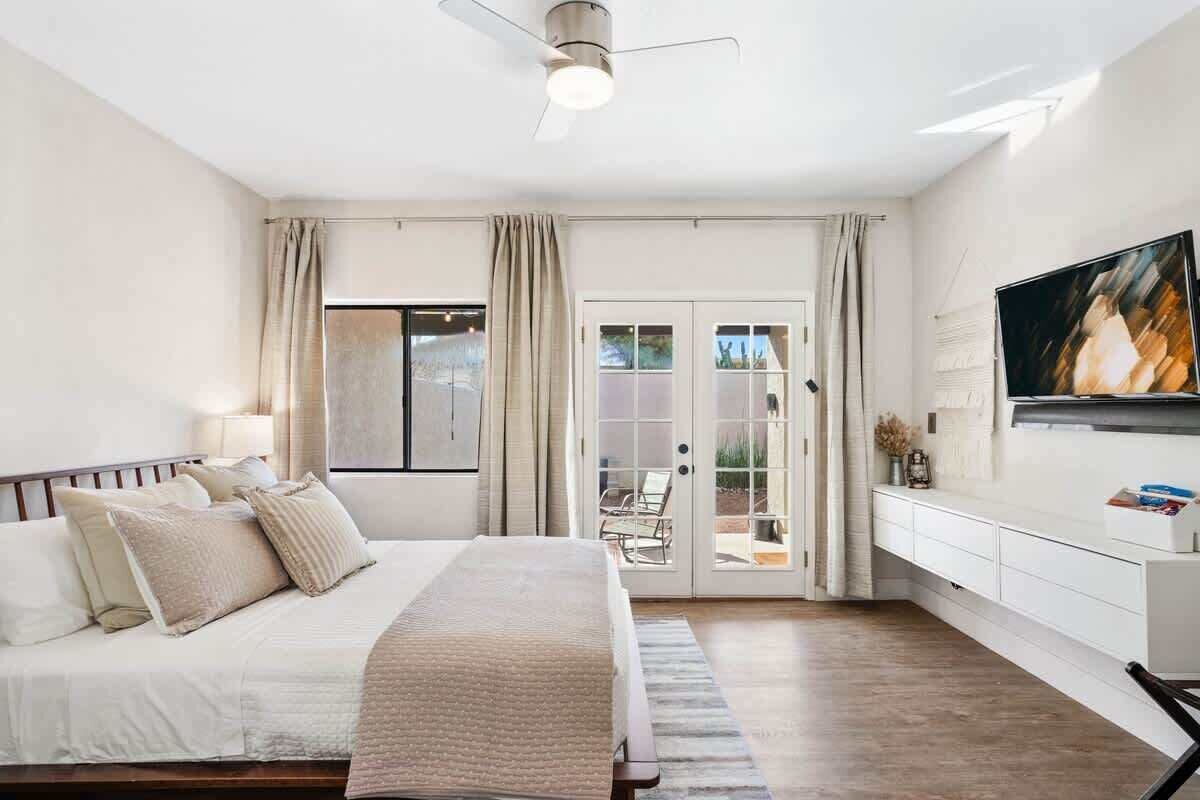 A bedroom with a bed, curtains, a ceiling fan, a TV, and a sliding glass door leading to an outdoor area.