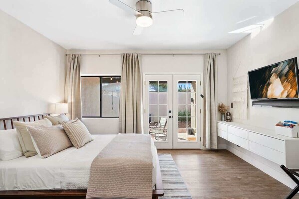 A bedroom with a bed, curtains, a ceiling fan, a TV, and a sliding glass door leading to an outdoor area. - Pool & Pet Friendly-Walk to Udall Park (Tucson)