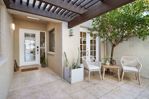 A covered patio area with a door, two wicker chairs, a small table, and a potted plant. - Pool & Pet Friendly-Walk to Udall Park (Tucson)