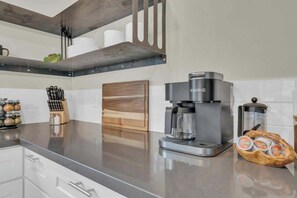 Eine Küche mit einer Keurig-Kaffeemaschine, einer Glaskaraffe, einer Korb mit Gebäck und einem Messerblock.
