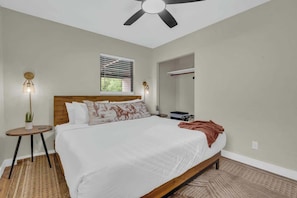 A bedroom with a bed, a ceiling fan, a window with blinds, a bedside table with a lamp, and a mirror. - The Hidden Gem-5 mins to U of A with Hot Tub (Tucson)