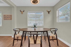 A dining area with a round table, six chairs, two bull horns on the wall, and a window with blinds. - The Hidden Gem-5 mins to U of A with Hot Tub (Tucson)