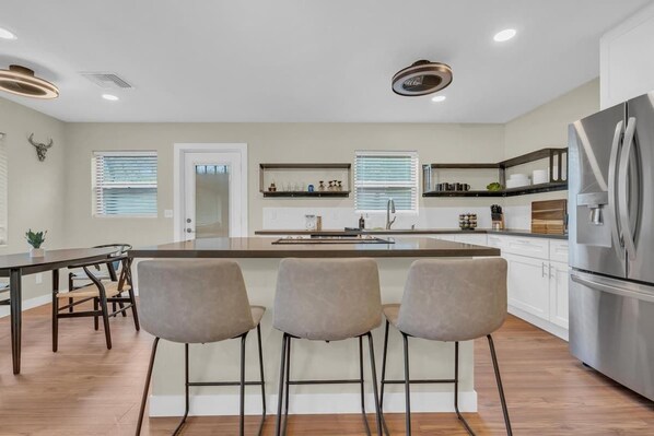 A modern kitchen with a central island, bar stools, a refrigerator, and built-in shelves. - The Hidden Gem-5 mins to U of A with Hot Tub (Tucson)