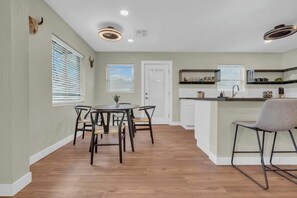 A modern kitchen with a central island, a dining area with a round table and chairs, and a small seating area with a chair. - The Hidden Gem-5 mins to U of A with Hot Tub (Tucson)