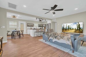 A modern living room with a sofa, a TV, and a dining area with chairs. - The Hidden Gem-5 mins to U of A with Hot Tub (Tucson)