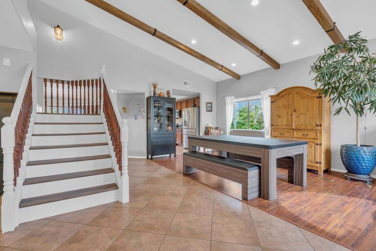 A spacious interior with a wooden staircase, a dining area with a bench, and a large potted plant.