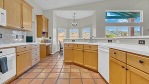 A kitchen with wooden cabinets, a white countertop, and a view of a desert landscape through large windows. - Catalina Mountain Views with Pool (Tucson)