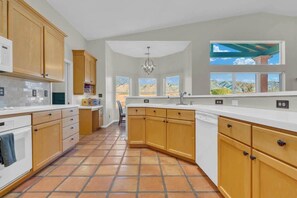 A kitchen with wooden cabinets, a white countertop, and a view of a desert landscape through large windows. - Catalina Mountain Views with Pool (Tucson)