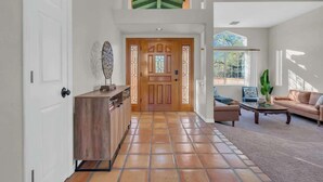 A spacious living area with a high ceiling, a wooden door, a sofa, a coffee table, and a view through a window. - Catalina Mountain Views with Pool (Tucson)