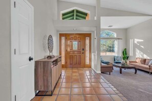 A spacious living area with a high ceiling, a wooden door, a sofa, a coffee table, and a view through a window. - Catalina Mountain Views with Pool (Tucson)