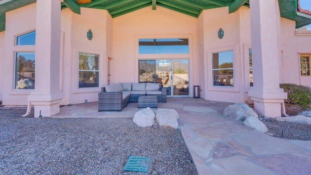 A covered outdoor seating area with a sofa and a table, a stone pathway, and a building with large windows and a green roof. - Catalina Mountain Views with Pool (Tucson)
