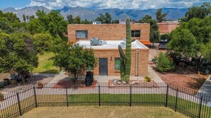 A brick building with a large cactus in front, surrounded by greenery and mountains in the background. - Trendy Cozy Townhome with Pool (Tucson)