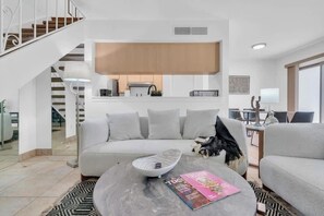 A modern living room with a grey sofa, a coffee table with a magazine, and a staircase leading to an upper floor. - Trendy Cozy Townhome with Pool (Tucson)